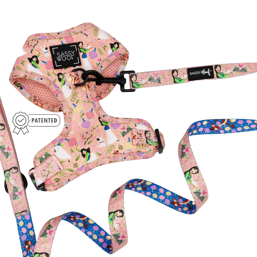 A Sassy Woof Dog Two Piece Bundle – Disney’s Mulan features a pink women, cats, and flowers patterned adjustable harness and leash set. A blue floral leash is also shown. Includes “Patented” badge and Puppy Growth Pawtection Plan for comfort.