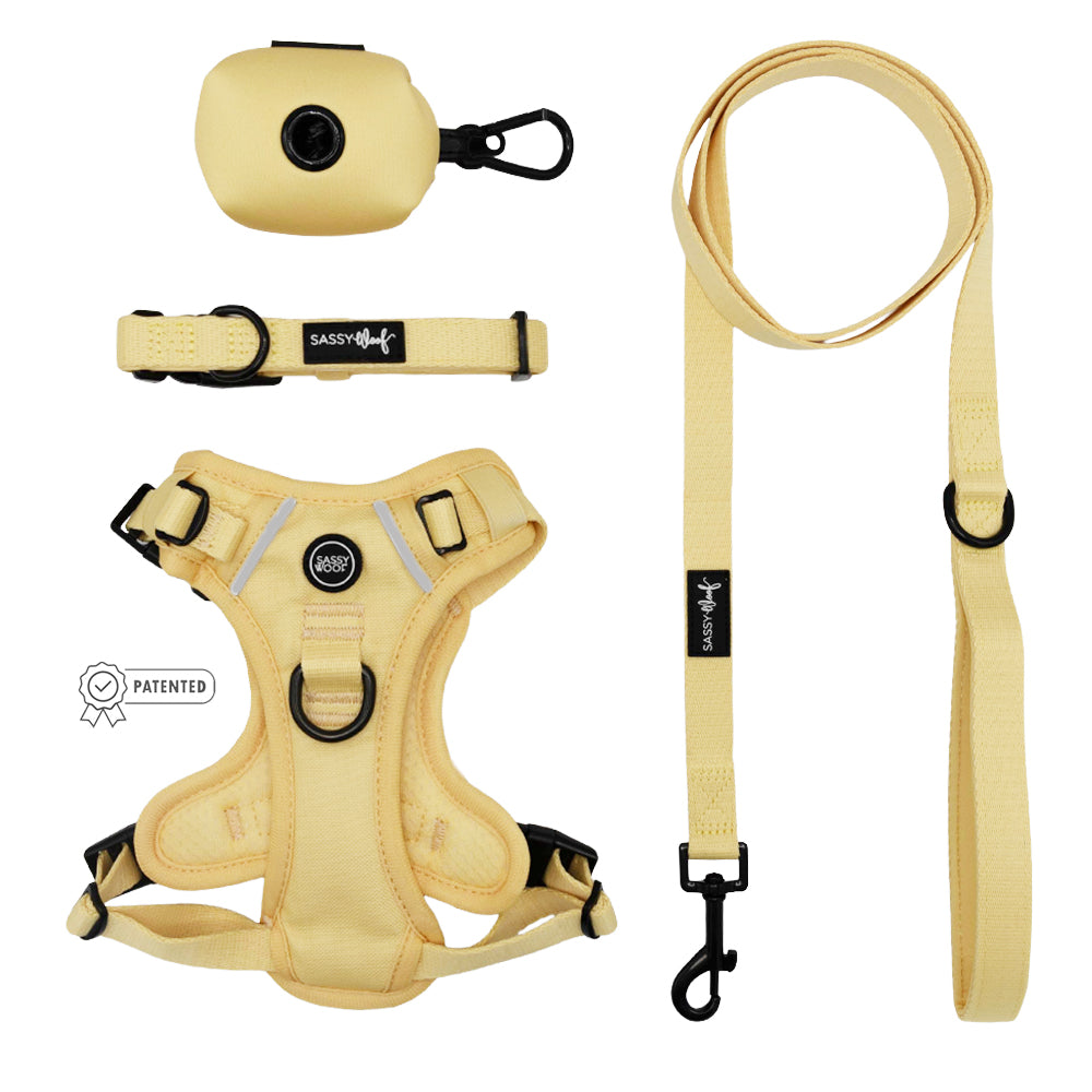 The Sassy Woof Dog Four Piece Bundle - Daffodil features a pale yellow harness, leash, collar, and waste bag dispenser on a white background. A small patent symbol appears near the harness.