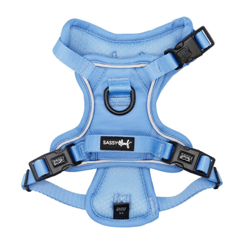 The Sassy Woof Dog Step-in Harness - Hydrangea is a light blue padded harness with adjustable reflective straps, black buckles, a metal leash ring, an Air Tag pocket, and the Sassy Woof logo on the front.