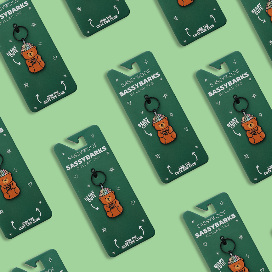 Green Sassy Woof Collar Tag - Hug Me Bear keychains, featuring an orange dog in a green hat, are displayed on green cards with “Sassy Woof Sassy Barks” and “Best Gift Ever.”.