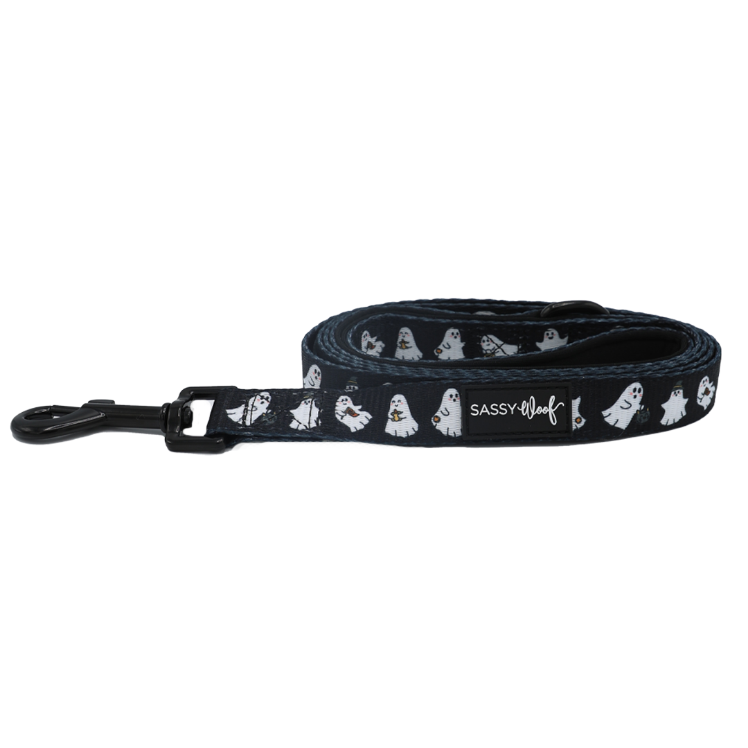 The Dog Leash - Lil Boo Thing by Sassy Woof is a rolled-up black dog leash adorned with white ghost illustrations and finished with a black clasp. As part of the Lil Boo Thing Dog Collection, this Halloween leash also displays an official Sassy Woof label.