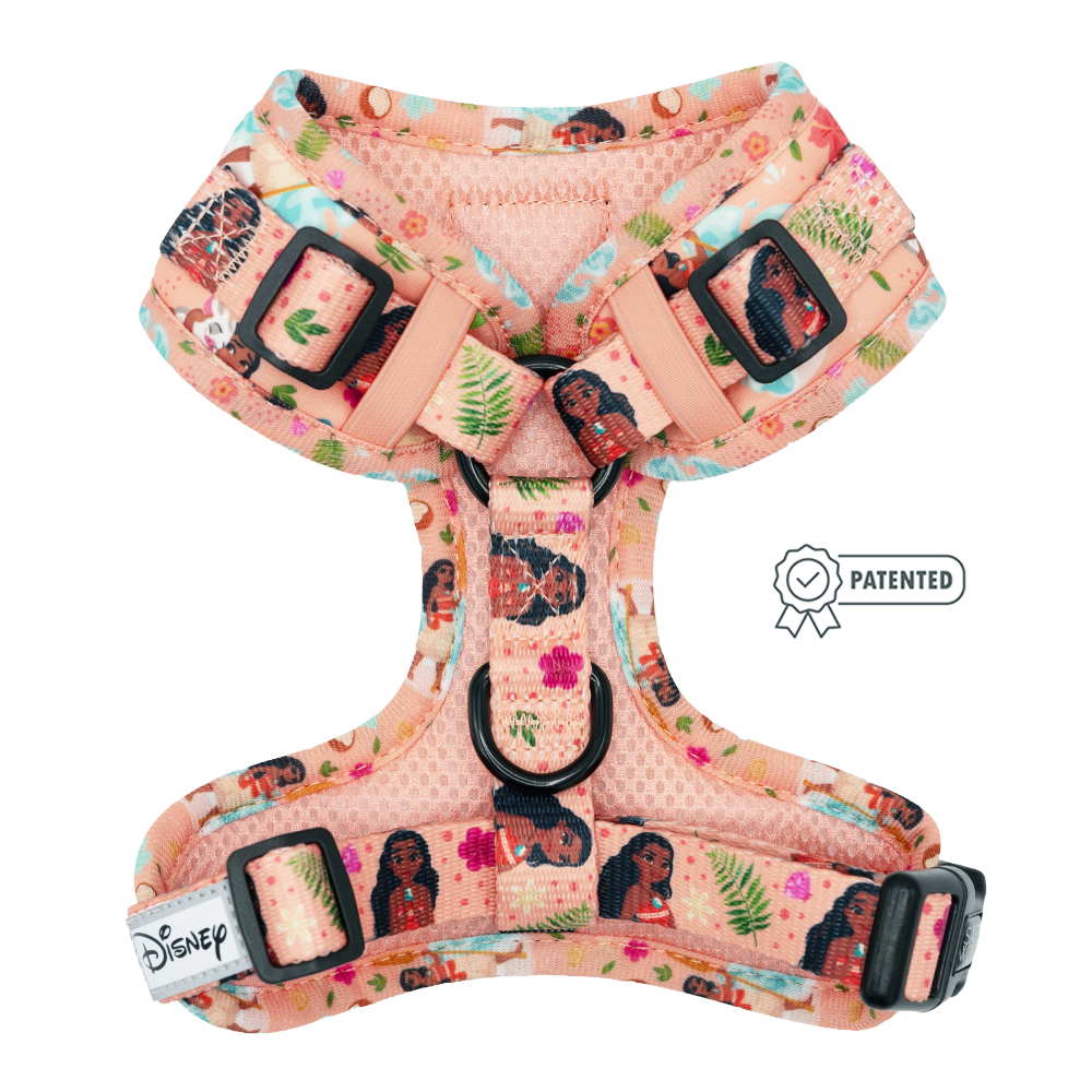 The Dog Adjustable Harness - Disney's Moana by Sassy Woof is peach-colored with tropical leaves, flowers, and ocean motifs. It features adjustable straps, black buckles, a no pull D-ring, patented badge, and Disney tag.