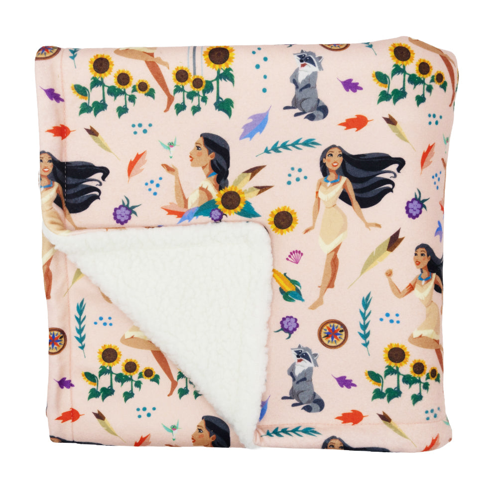The Sassy Woof Pet Blanket - Disney's Pocahontas features a soft, folded design with illustrated women, raccoons, sunflowers, colorful leaves, and feathers on a light pink background; the reverse side is white and fluffy.