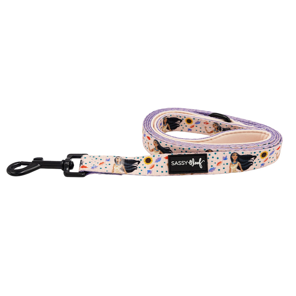 The Sassy Woof Dog Leash - Disney's Pocahontas features a vibrant pattern inspired by Pocahontas with women, sunflowers, and abstract shapes on a pale background, plus a black metal clip and Sassy Woof label. Adjustable harness and collar included.