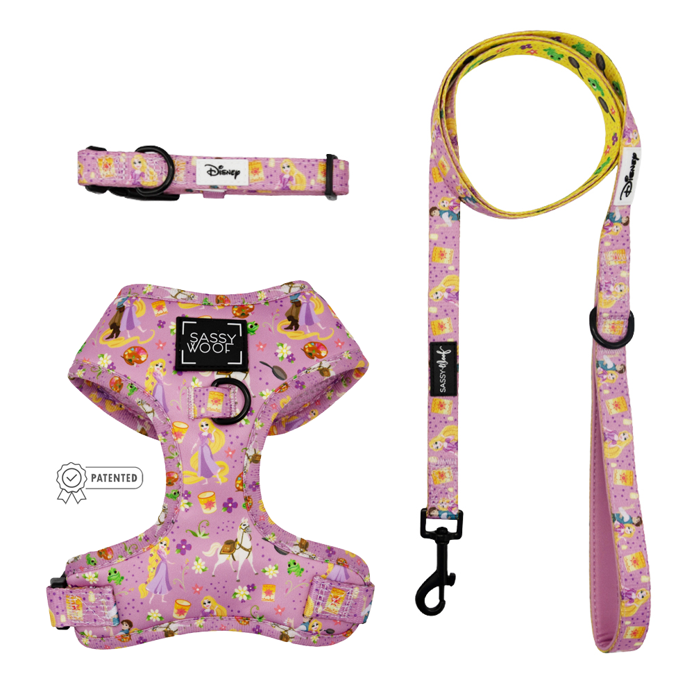 The Sassy Woof Harness Three Piece Bundle - Disney's Rapunzel includes a pink harness, collar, and leash with princesses and castles, shown on white. This Tangled-inspired set is perfect for your royal pup.