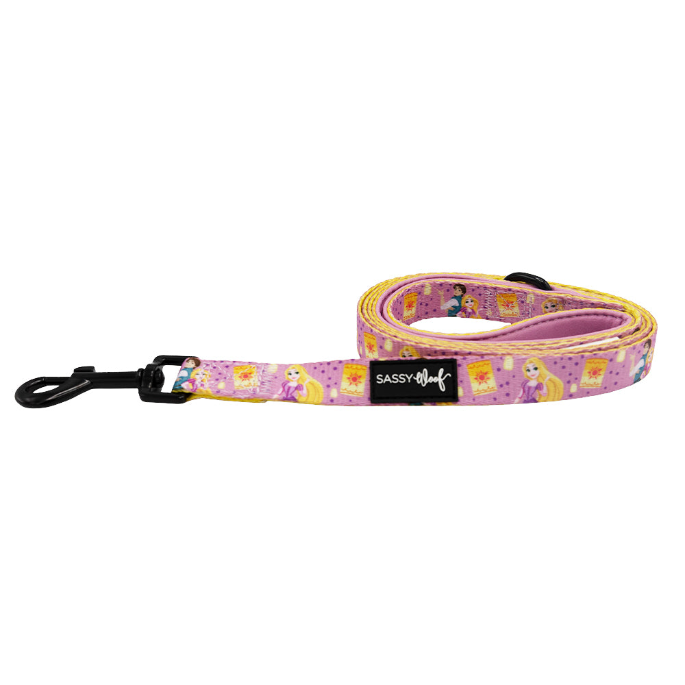 The Sassy Woof Dog Leash - Disney's Rapunzel features pink fabric with cartoon princess and yellow flower designs, a black metal clip, and Sassy Woof label—perfect for fans of Disney dog accessories.