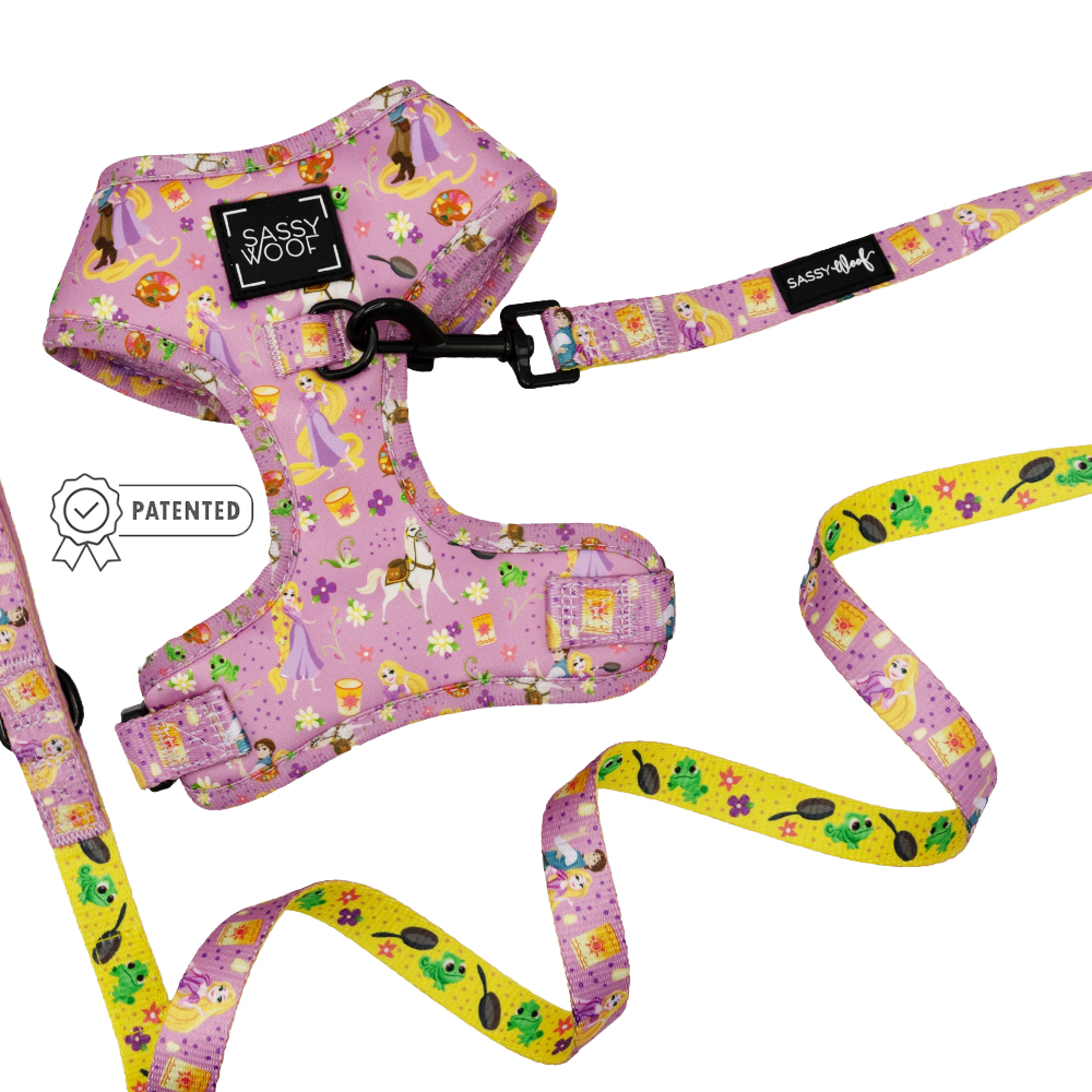 The Sassy Woof Dog Two Piece Bundle - Disney's Rapunzel features a pink harness and yellow leash with fairy tale and princess designs, perfect for Tangled fans. The harness displays a Patented badge icon.