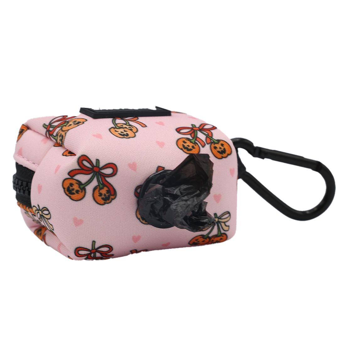 The Dog Waste Bag Holder - Sassy Lil Pumpkins by Sassy Woof is a pink dispenser from the Sassy Lil Pumpkins Dog Collection, accented with a black clip and adorned with playful cartoon gingerbread cookies and hearts. A black poop bag is partially pulled out of the dispenser opening, making this holder a charming and practical addition to any pumpkin-themed dog accessories.