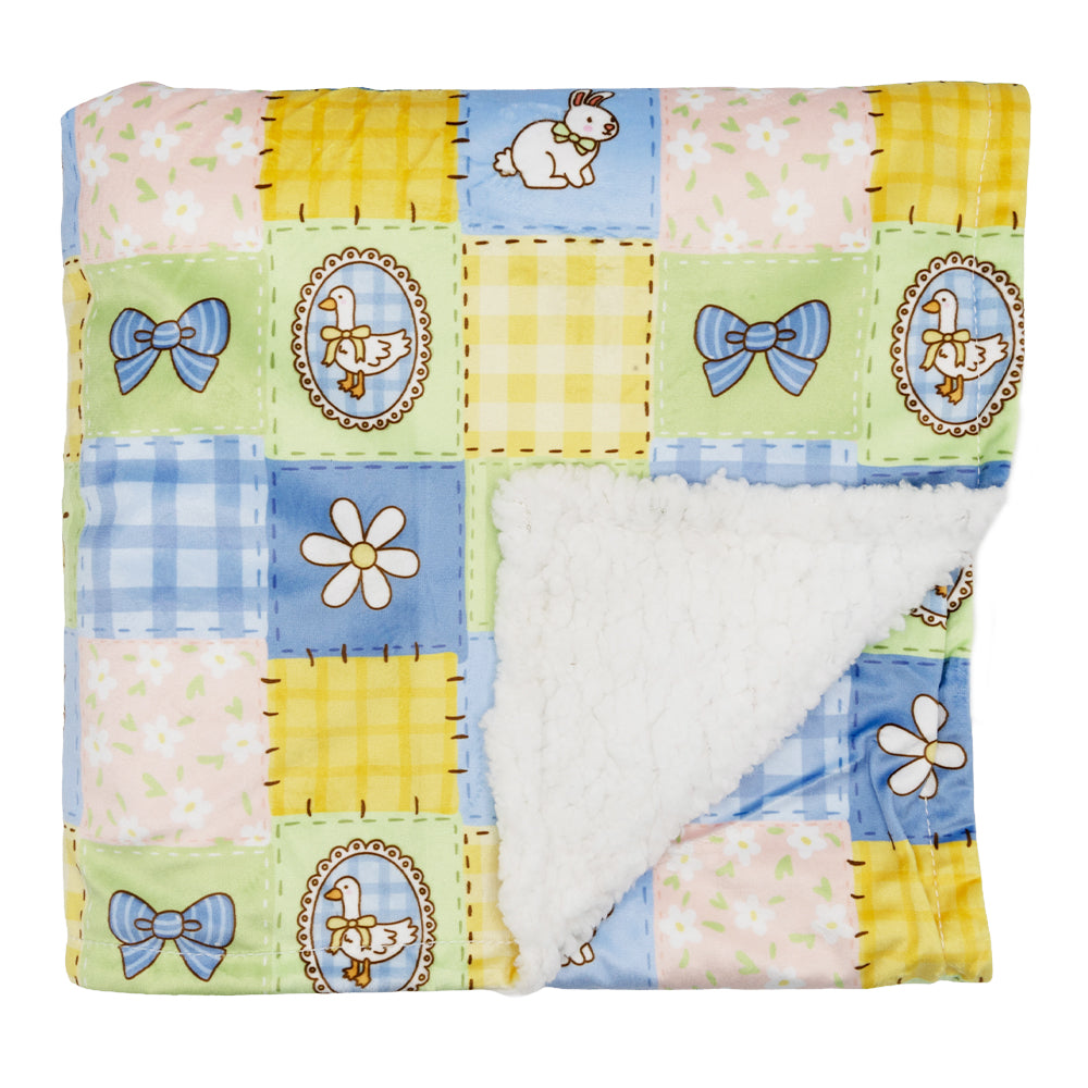 The Sassy Woof Pet Blanket - Patch Perfect features a quilted patchwork of pastel squares, bows, flowers, and bunny designs. One corner folds over to reveal a plush white polyester lining for extra softness.