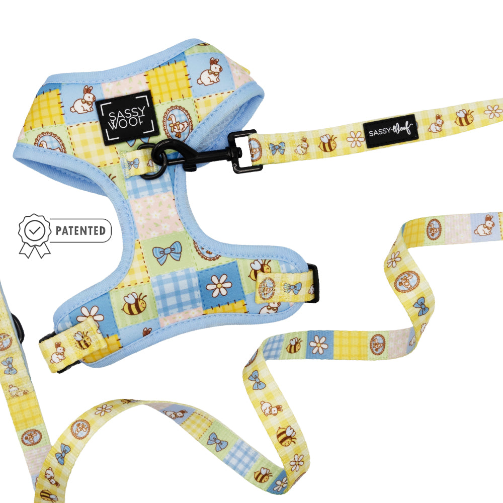The Sassy Woof Dog Two Piece Bundle - Patch Perfect features a pastel blue and yellow adjustable harness and leash with a cute bunny, bee, flower, bow, and egg patchwork design plus a patented badge on the left side.