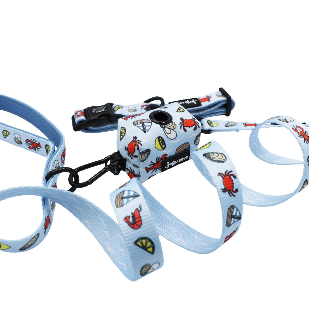 The Sassy Woof Dog Three Piece Bundle - Coastal Cuties features a light blue leash, collar, and matching waste bag holder with playful red crabs, lobsters, lemon slices, and shells on a white background.