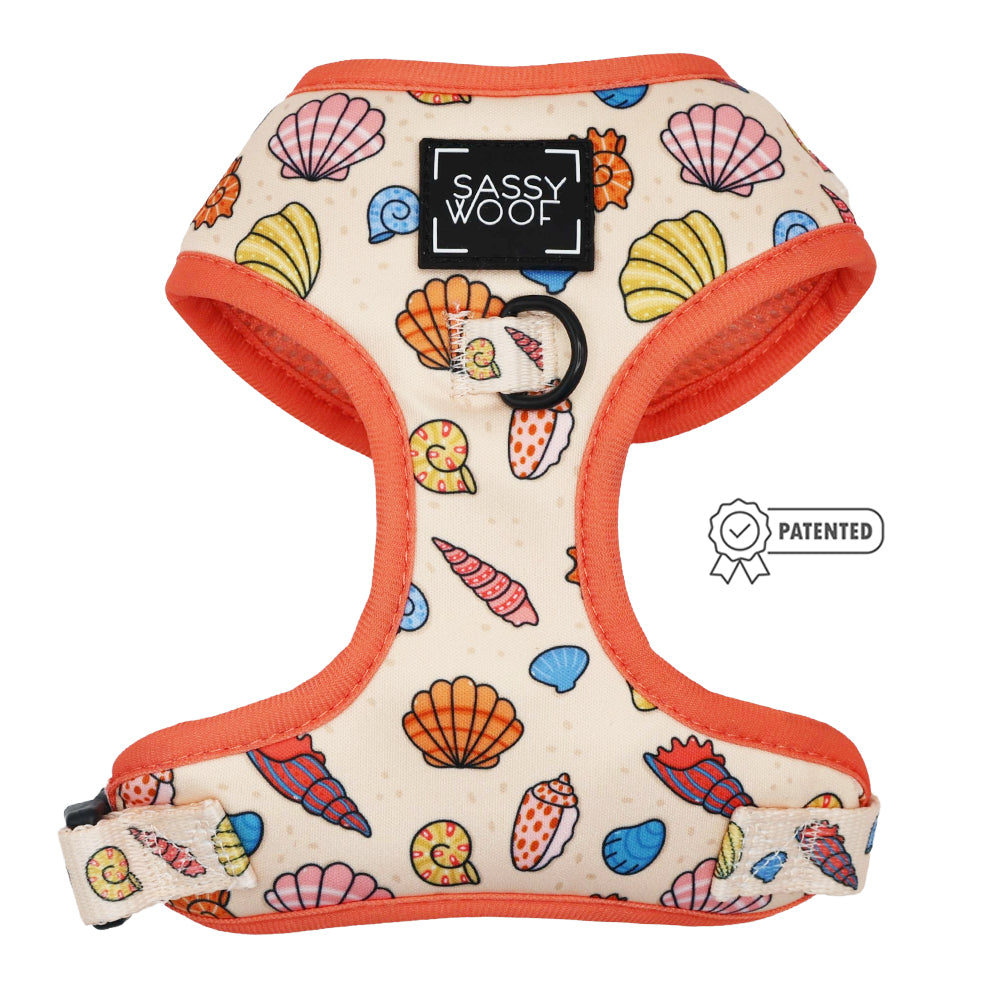 The Shell Yeah Dog Adjustable Harness by Sassy Woof features a colorful seashell pattern, orange trim, front logo patch, puppy growth protection, and a patented badge on the right side.