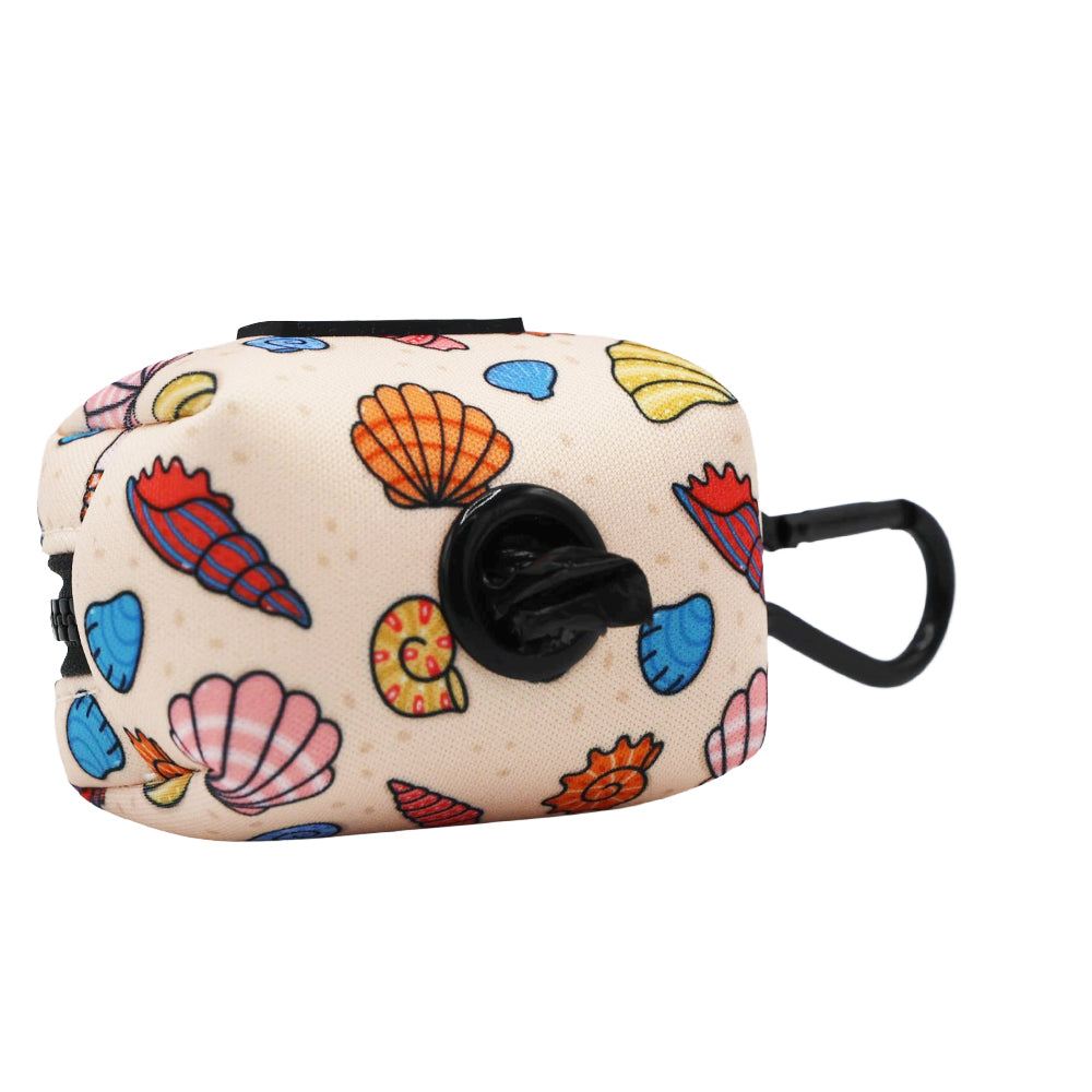 The Sassy Woof Dog Waste Bag Holder - Shell Yeah features colorful seashell patterns on beige, a black plastic clip, and a circular opening with a black bag—perfect for beachy adventures with your pup.