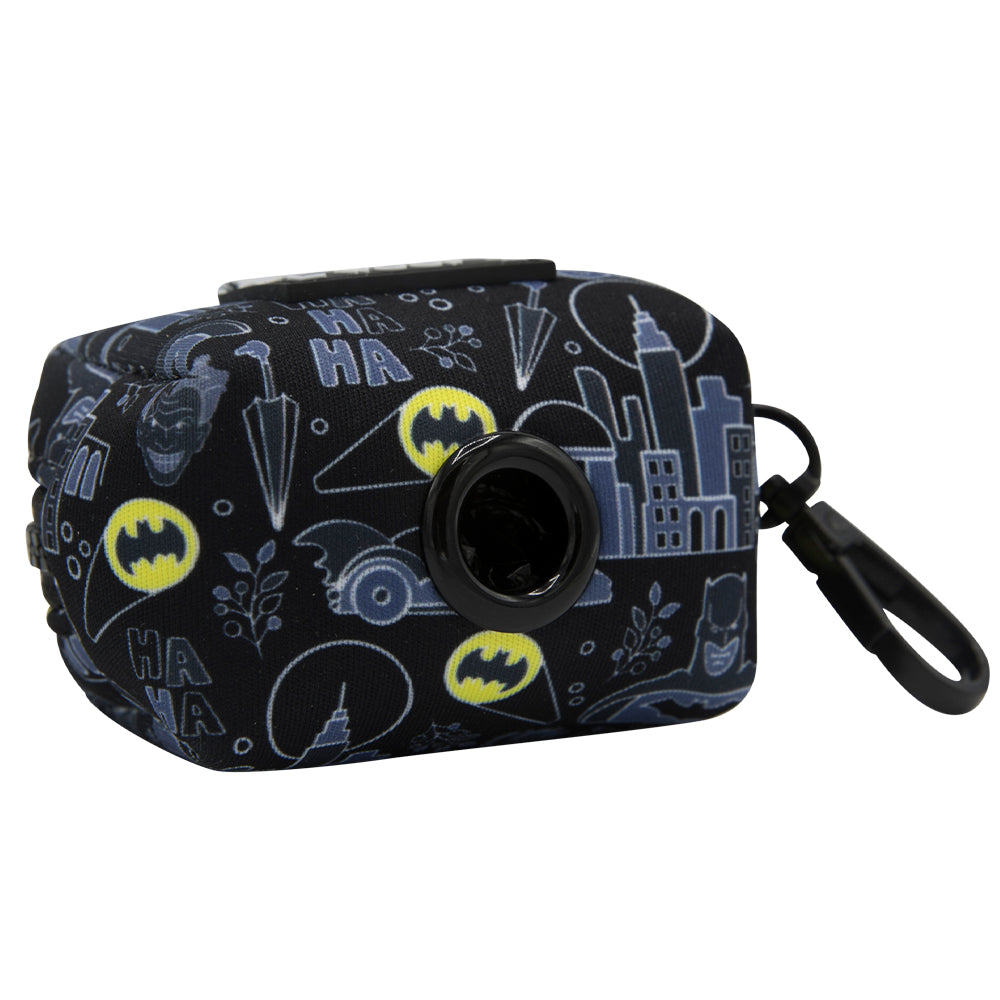 The Sassy Woof Dog Waste Bag Holder - Batman™ features a dark fabric with yellow Batman logos, cityscapes, and comic elements. Includes a dispenser opening and black clip; pairs perfectly with the matching adjustable harness.