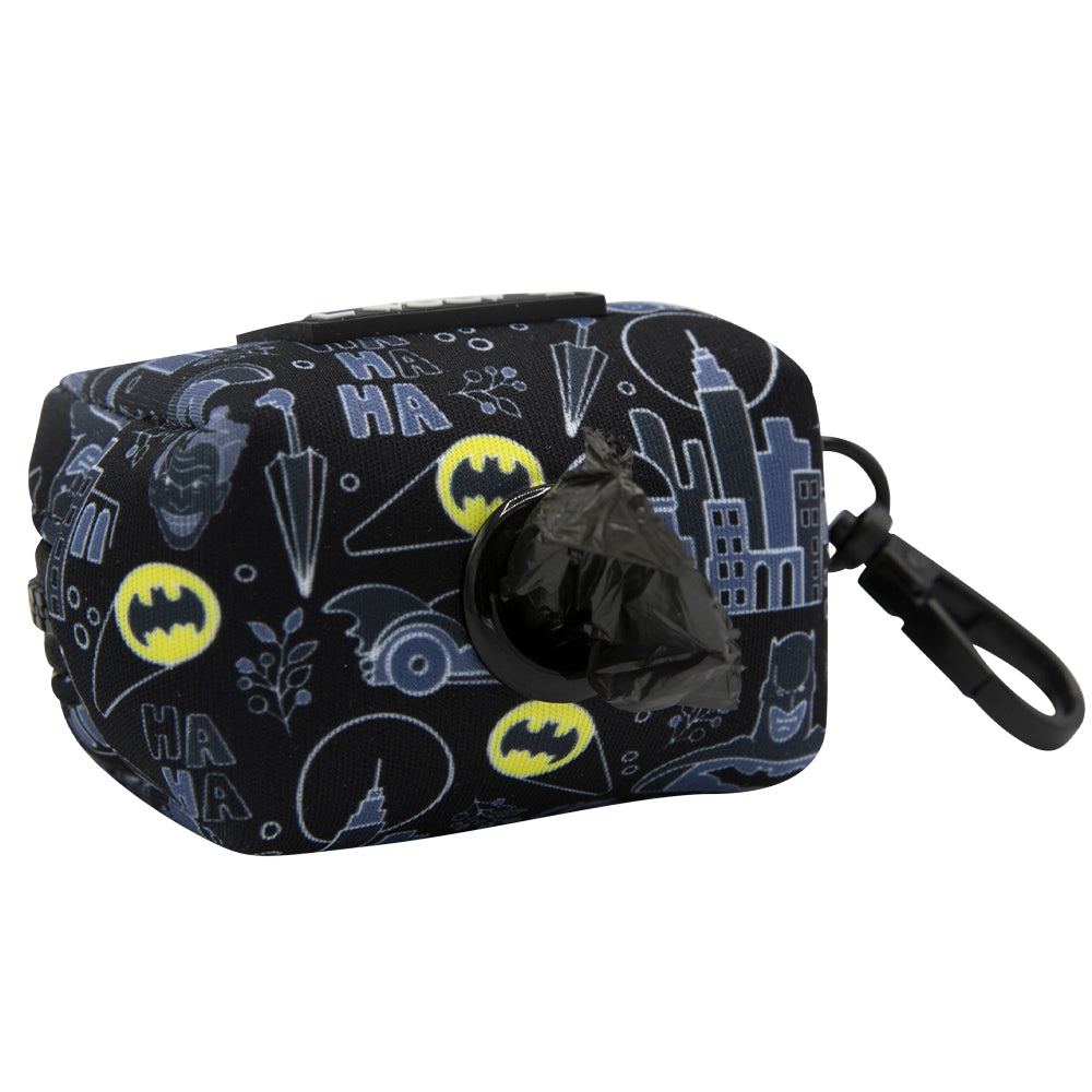 The Sassy Woof Dog Waste Bag Holder - Batman™ is a black fabric holder featuring yellow Batman logos, comic graphics, and cityscape outlines. Includes a roll of black waste bags and a clip for attaching to any adjustable harness.