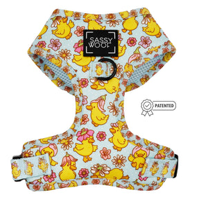 The Sassy Woof Dog Adjustable Harness - Good Duck, Babe! is a light blue harness with yellow cartoon ducks and pink flowers. It features a Sassy Woof label, metal leash ring, and an adjustable strap with patented design badge.
