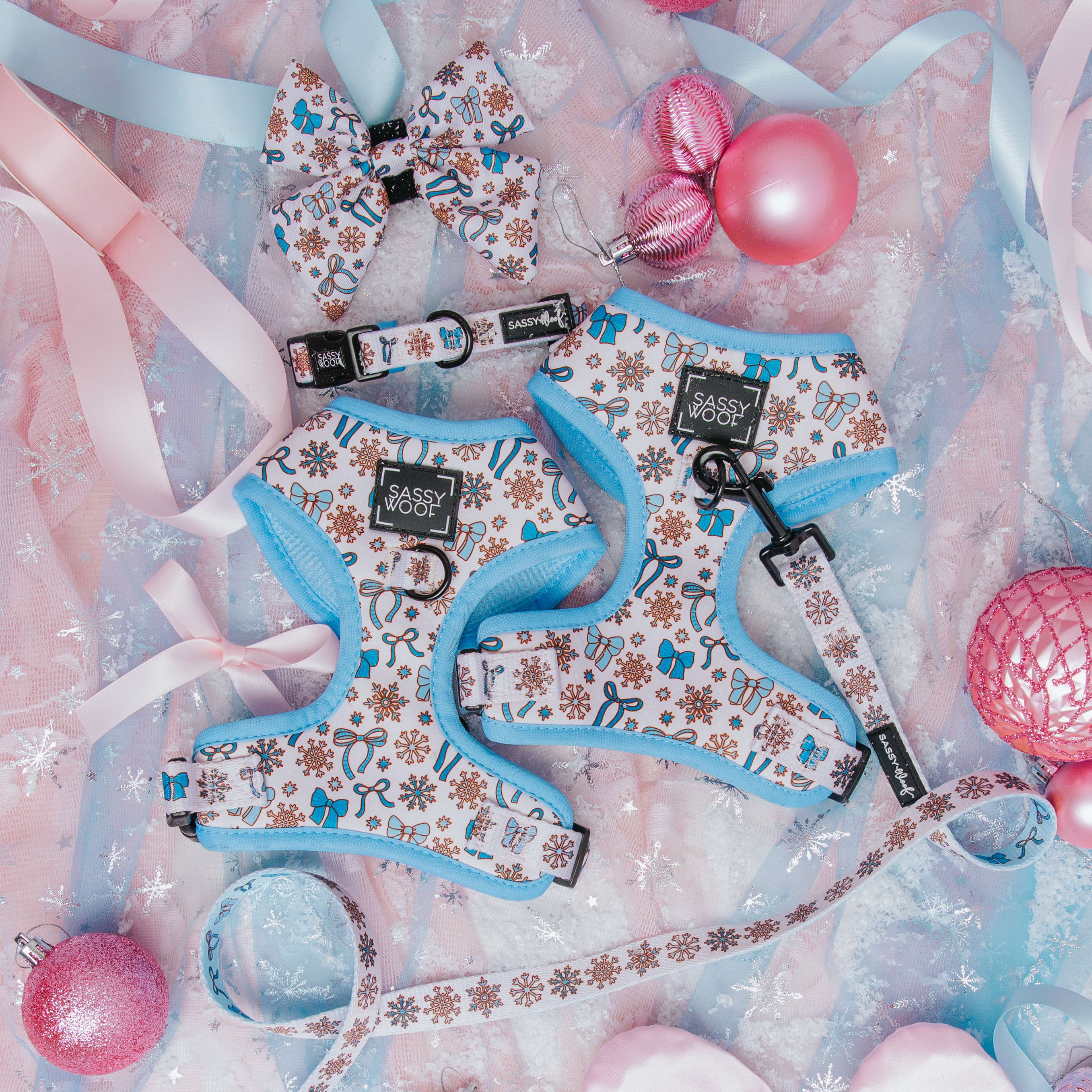 Dog harness, leash, and bow tie set with decorative ribbons and balls on a soft pink background.