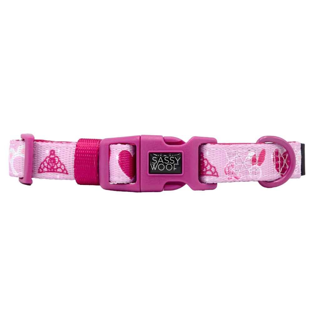 The Sassy Woof Dog Collar - Mean Girls™ is a pink adjustable collar with a plastic buckle, featuring tiara and heart designs and the Sassy Woof brand on the clasp.