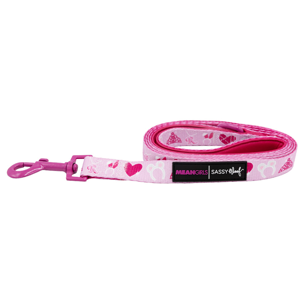 The Sassy Woof Dog Leash - Mean Girls™ features pink heart and crown patterns, a metal clip, and a black MEAN GIRLS SASSY WOOF label—perfect to pair with matching accessories. Shown coiled on a white background.