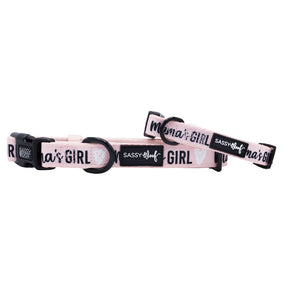 The Sassy Woof Dog Collar - Mama's Girl is a pink, adjustable neoprene collar with black hardware, "mamas GIRL" text, white heart designs, and a SASSY WOOF label—offering both comfort and style.