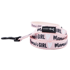 The Sassy Woof Dog Leash - Mama's Girl features a soft neoprene handle, black hardware, and "Mamas GIRL" with white hearts on pink. It includes a black Sassy Woof label and pairs well with an adjustable harness or matching dog collar.