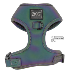 The Sassy Woof Dog Adjustable Harness - Reflection features an iridescent green and purple finish, reflective material for nighttime safety, adjustable straps, black buckle closures, a front logo, and a patented side symbol.