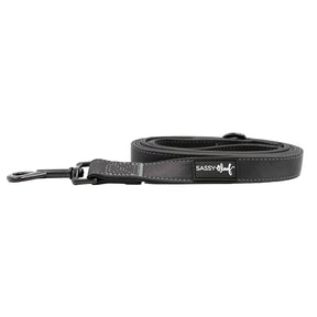 The Sassy Woof Dog Leash - Reflection is a black reflective leash with white stitching, padded handle, and metal clasp—ideal for nighttime dog safety.