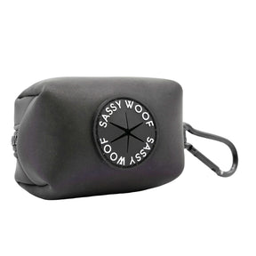 The Sassy Woof Dog Waste Bag Holder - Reflection is a black neoprene holder with a round logo, side zipper, and black clip—ideal for nighttime walks when paired with reflective dog accessories.