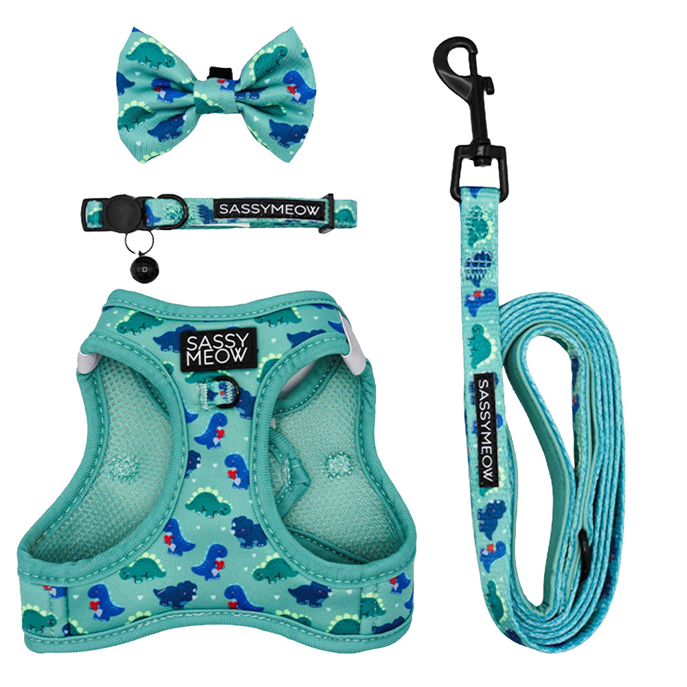 The Cat Bundle - Dino Darling by Sassy Woof features an aqua blue harness, leash, collar, and bow tie with cartoon dinosaur prints. Adjustable for cats or small pets.