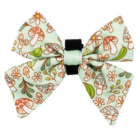 The Sassy Woof Dog Sailor Bow - Shrooms & Blooms features red and blue mushrooms, green leaves, and flowers on a light green background with a black center band—perfect for accessorizing any dog collar or harness.