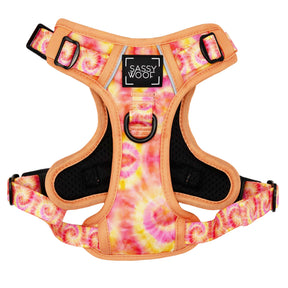 The Sassy Woof Dog Step-in Harness - Summer Sorbet features orange, pink, and yellow tie-dye patterns, a black inner lining, adjustable reflective straps, a metal leash ring, and a Sassy Woof label on the chest.