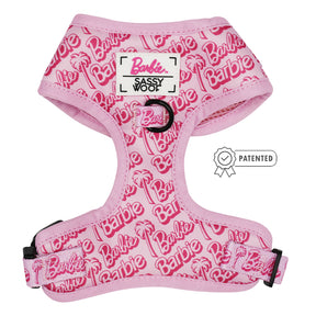The Dog Adjustable Harness - BARBIE™ Malibu by Sassy Woof features pink fabric with repeated Barbie logos and palm trees, plus a Sassy Woof label and patented badge. It's adjustable and part of the exclusive Barbie x Sassy Woof collection.