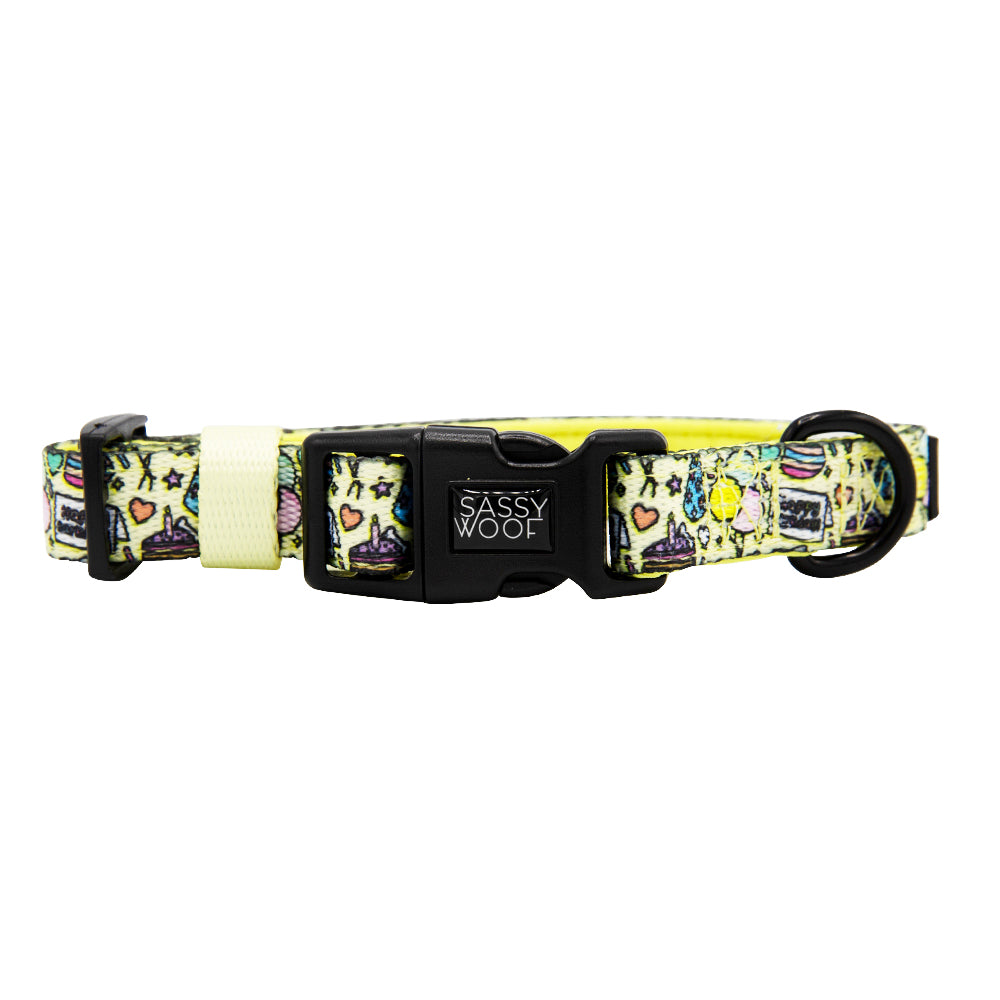 The Sassy Woof "Raise the Woof" dog collar features a light yellow background with playful doodles, an adjustable neoprene strap, and a black plastic buckle with the Sassy Woof logo plus a sturdy D-ring.