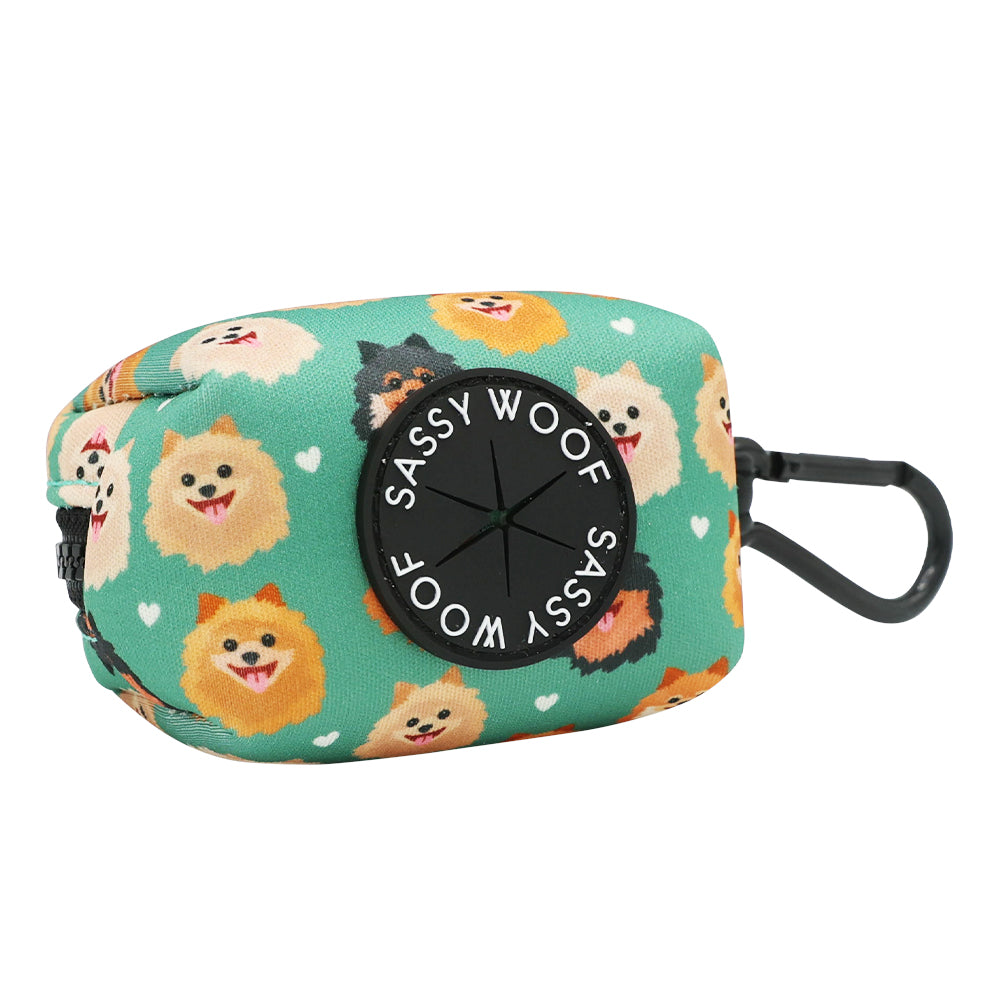 The Sassy Woof Dog Waste Bag Holder - Pawfect Poms is a teal neoprene accessory with cartoon Pomeranian faces, white hearts, a black dispenser, and clip—ideal to pair with the matching dog harness.