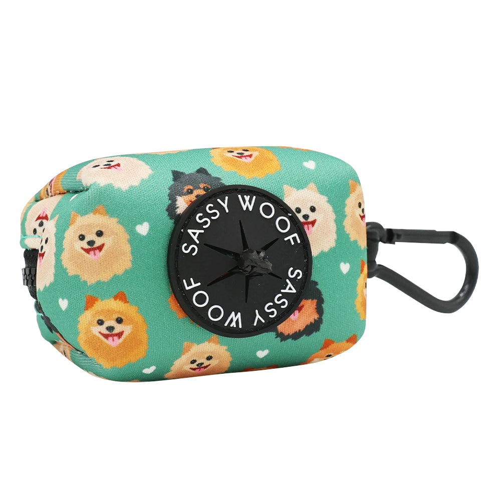 The Sassy Woof Dog Waste Bag Holder - Pawfect Poms is a green rectangular neoprene accessory with a black clip, cartoon Pomeranian faces, and white hearts—a stylish match for your dog harness.