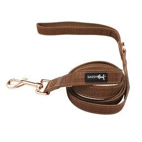 The Sassy Woof Dog Leash - Teddy, from the brown collection, features a neoprene handle, metal clasp, and a black Sassy Woof label. It is shown neatly coiled on a white background.