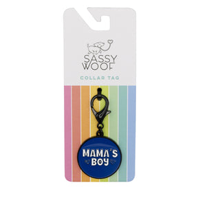 The Sassy Woof Dog Collar Tag - Mama's Boy is a round blue charm with white lettering, attached to a black clasp and displayed on rainbow-striped packaging.