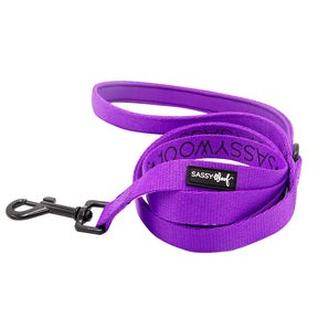 The Sassy Woof Dog Leash - Neon Purple features a coiled, padded handle, black metal clip, and a “Sassy Woof” label near the handle, shown against a white background.