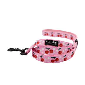 The Sassy Woof Dog Leash - Mon Chérry features pink fabric with cherries and a padded handle for comfort. Pair it with the matching adjustable harness for a coordinated, sweet style.