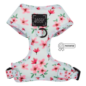 The Sassy Woof Dog Adjustable Harness - Sakura features a pink cherry blossom design with black buckles and an adjustable fit. A small patented badge appears next to the harness.