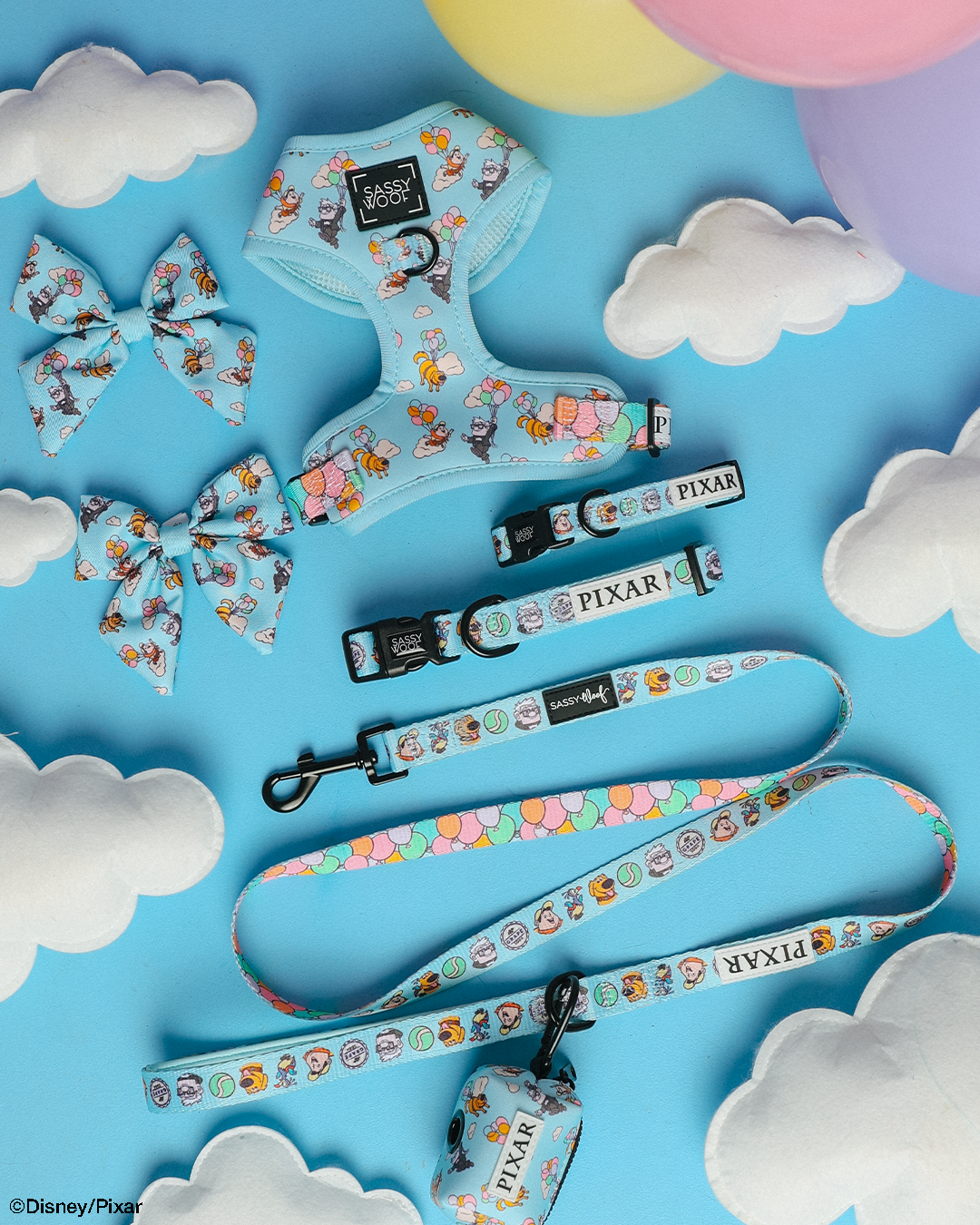 Light blue dog harness, collar, leash, two bows, and a waste bag holder featuring colorful Pixar’s Up characters, displayed on a sky-blue background with clouds and pastel balloons.