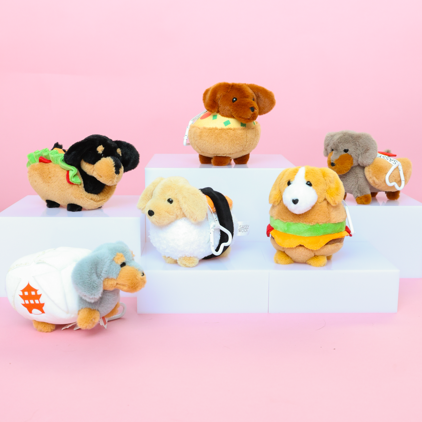Six plush toy dogs dressed as different foods, including a taco, hamburger, sushi, and hot dog, displayed on white steps against a pink background.