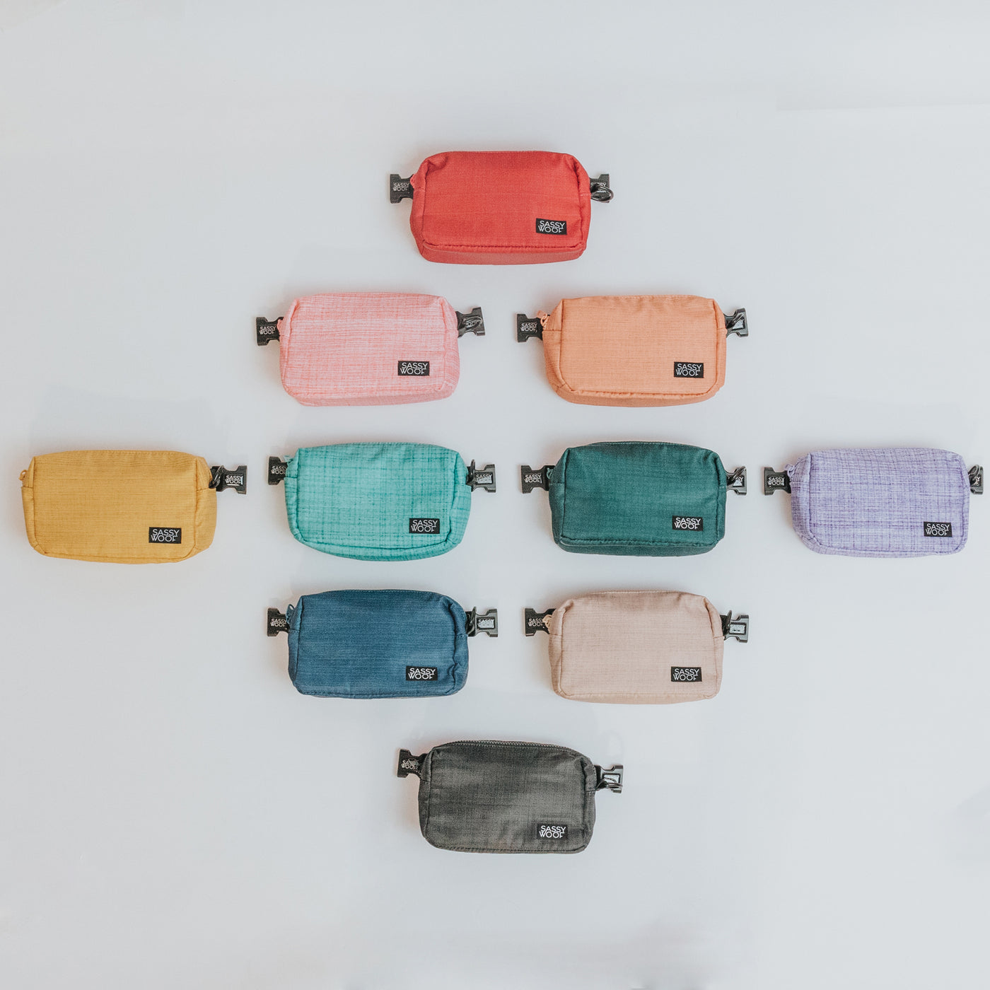 Ten small rectangular pouches in various colors are neatly arranged in rows on a white background. Each pouch has a zipper and a black label on the lower corner.