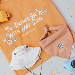 Flat lay of Sassy Woof’s Human Tee - I’d Rather Be With My Dog (printed with eco-friendly ink), dog mom bucket hat, blue & orange bandanas, and a floral orange dog harness on a light surface.