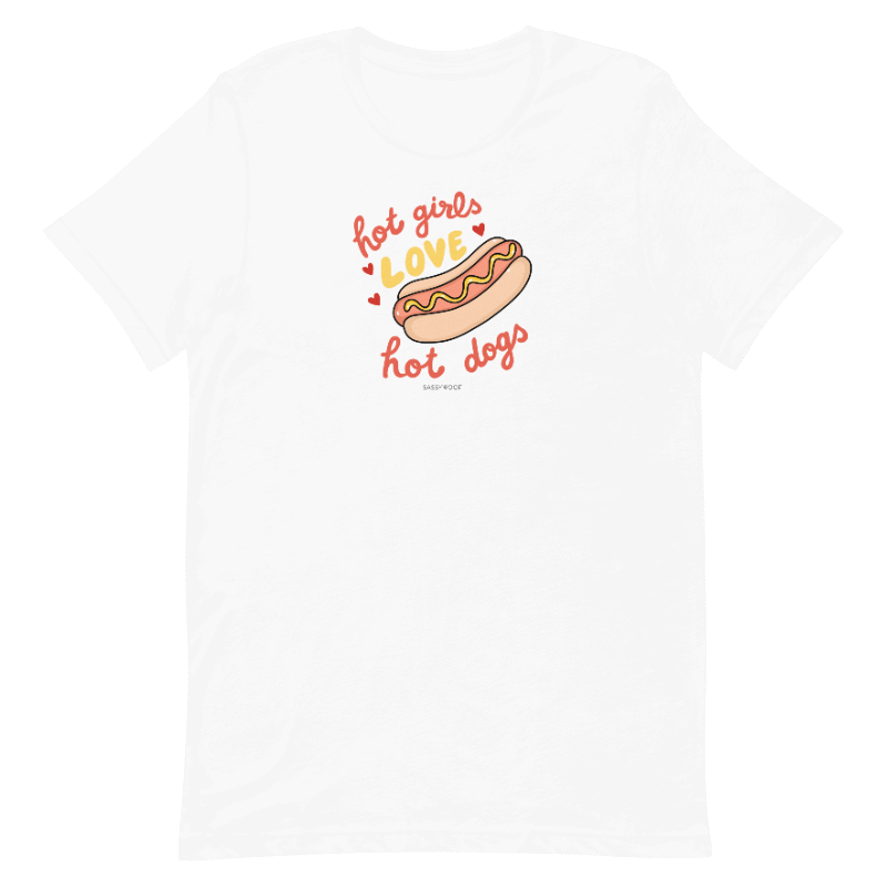 The Sassy Woof Hot Girls Love Hot Dogs Tee is a white unisex t-shirt with a fun hot dog graphic and playful “hot girls love hot dogs” text in red and orange, printed using eco-friendly ink.