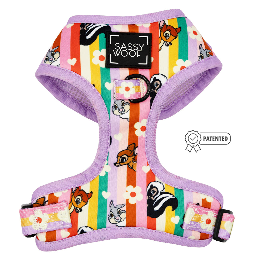 The Sassy Woof Dog Adjustable Harness – Disney’s Bambi features purple trim, rainbow stripes, and cartoon animal faces like a cat, dog, and skunk. This no-pull harness has a Sassy Woof label with a patented badge beside it.