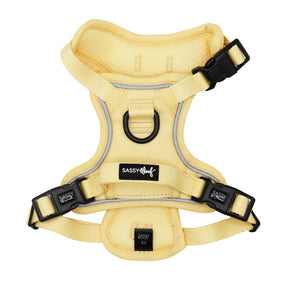 The Sassy Woof Dog Step-in Harness - Daffodil features yellow reflective material, black plastic buckles, adjustable straps, an AirTag pocket, a metal top-center D-ring, and brand labels. The harness is displayed flat on a white background.