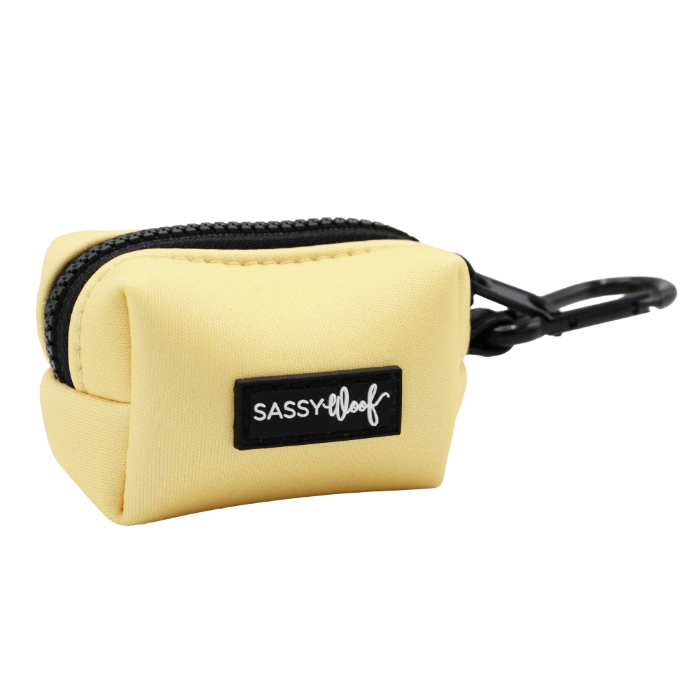 The Sassy Woof Dog Waste Bag Holder - Daffodil is a small, yellow fabric pouch with a black zipper, plastic clip, and a black label reading "SASSY WOOF" in white—perfect for dog walks.