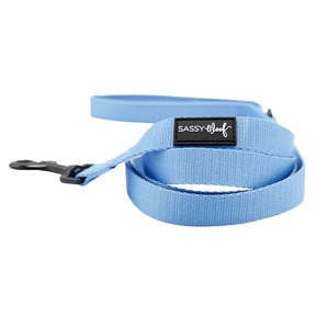 The Dog Leash - Hydrangea by Sassy Woof features a light blue pastel floral pattern, a black metal clasp, and a black Sassy Woof label in white. Neatly coiled, it’s perfect for your next walk with your pup.