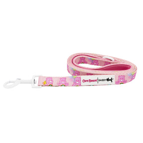 The Sassy Woof Dog Leash - Care Bears™ Cheer Bear is a pink padded leash with repeating Cheer Bear, hearts, and rainbows. It features a white clip, Care Bears | Sassy Woof label, and pairs perfectly with the matching harness.
